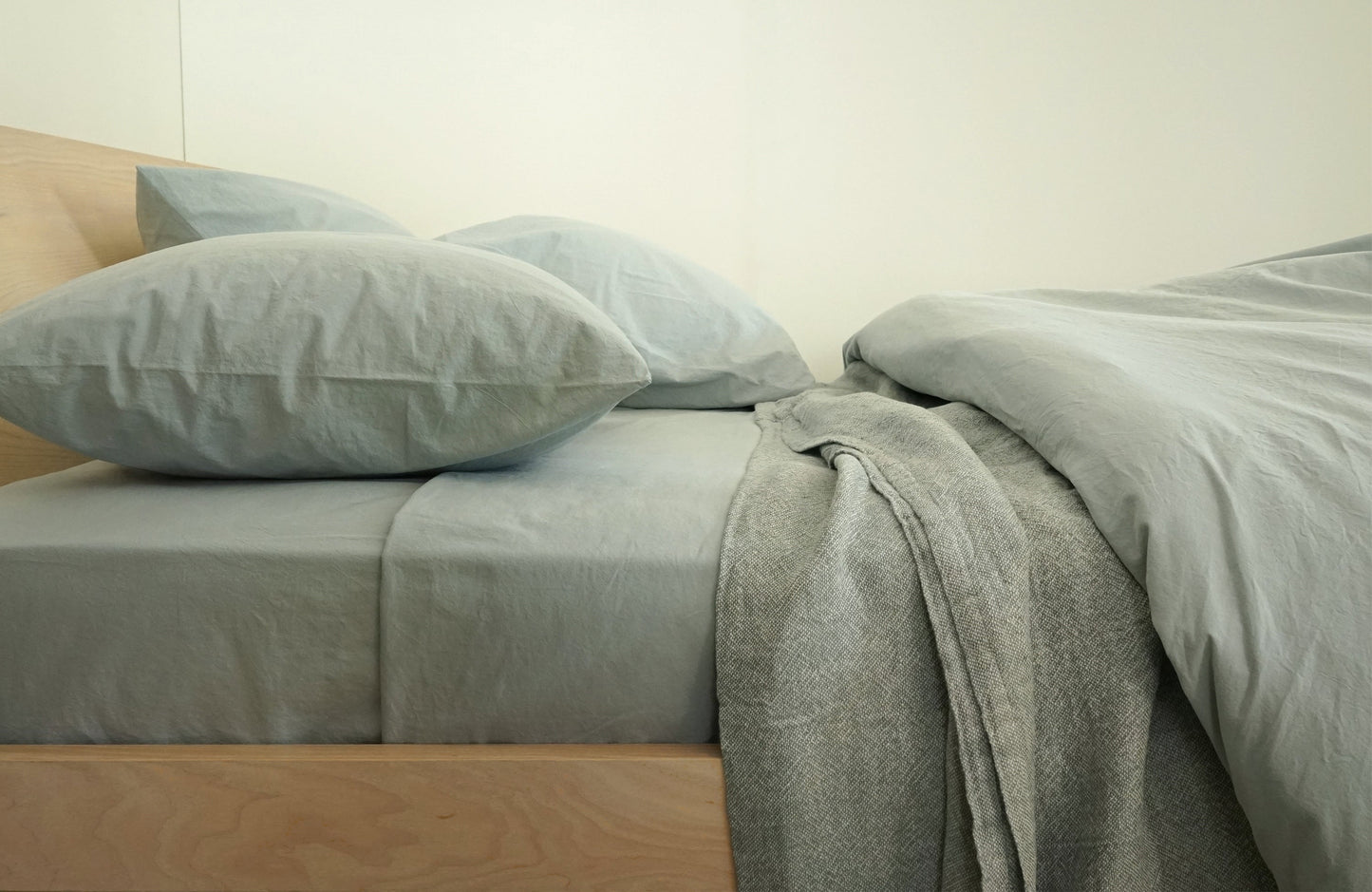 light blue mist colored sheets made from cotton percale on maple bed with lightweight linen blanket tucked under duvet